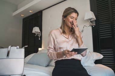 Otel odasında dijital tableti üzerinde çalışan genç iş kadınının portresi. İş seyahati kavramı.