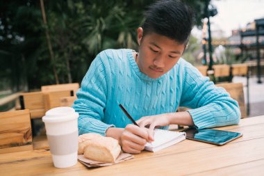 Dijital tabletini kullanan ve kahve dükkanında otururken not alan Asyalı genç bir adamın portresi.. 