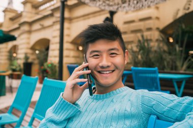 Bir kafede otururken telefonla konuşan Asyalı genç adamın portresi. İletişim konsepti.