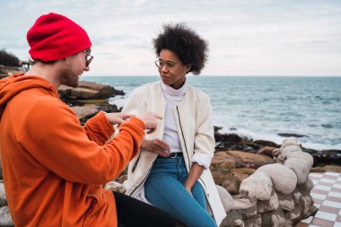 İki genç arkadaşın portresi, arka planda deniz otururken birlikte iyi vakit geçirip sohbet ediyorlar..