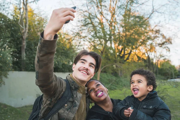 公園の屋外で携帯電話で楽しい時間を過ごしている素敵な混合人種の民族家族の肖像画 — ストック写真