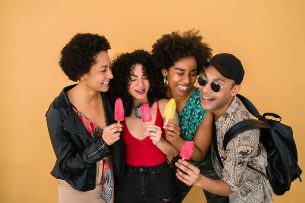 Portrait of multi-ethnic group of friends having fun and enjoying summertime while eating ice cream against yellow background.