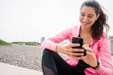 Eğitime ara verdiğinde cep telefonunu kullanan atletik bir kadının portresi. Spor ve sağlık yaşam tarzı.