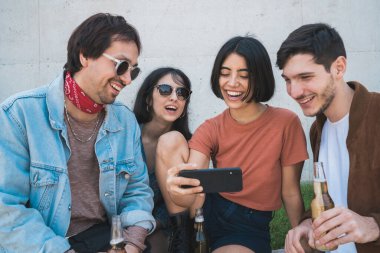 Açık havada akıllı telefondan bir şeyler izlerken birlikte zaman geçiren bir grup genç arkadaşın portresi. Teknoloji ve arkadaşlık kavramı.