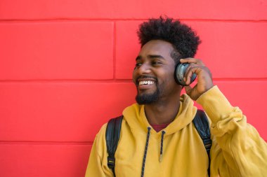 Kızıl arka planda kulaklıkla müzik dinleyen genç afro bir adamın portresi. Teknoloji konsepti.