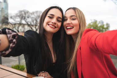 Kafede otururken selfie çeken iki genç arkadaşın portresi. Yaşam tarzı ve arkadaşlık kavramı.