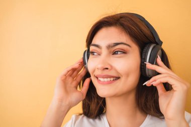 Sarı arka planda kulaklıkla müzik dinleyen genç Latin kadın portresi. Şehir konsepti.