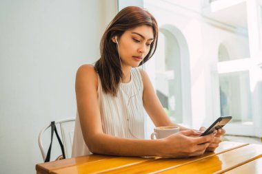 Kafede otururken cep telefonunu kullanan genç Latin kadının portresi. İletişim konsepti.