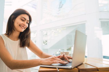 Bir kafede otururken dizüstü bilgisayarını kullanan genç Latin kadının portresi. Teknoloji ve yaşam tarzı kavramı.