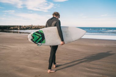 Genç sörfçü siyah sörf takımıyla okyanusta duruyor. Spor ve su sporları konsepti.