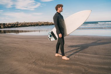 Genç sörfçü siyah sörf takımıyla okyanusta duruyor. Spor ve su sporları konsepti.