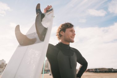 Plajda sörf tahtasıyla duran ve siyah sörf kıyafeti giyen genç sörfçünün yakın çekimi. Spor ve su sporları konsepti.