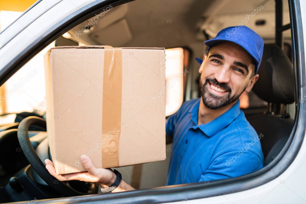 Portrait of a delivery man holding cardboard boxes in van. Delivery service and shipping concept.