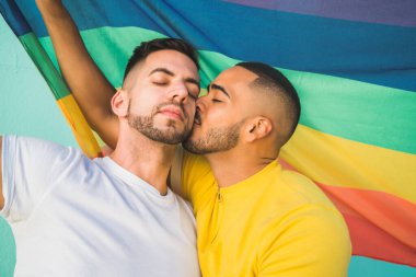 Sokakta gökkuşağı bayrağıyla sarılıp sevgilerini gösteren genç eşcinsel çiftin portresi. LGBT ve aşk konsepti