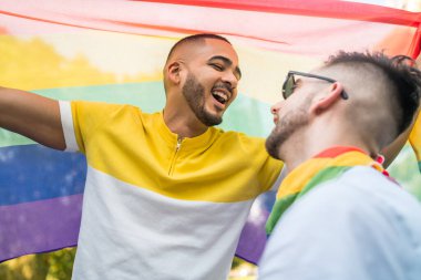 Genç eşcinsel çiftin portresi. Sokakta gökkuşağı bayrağıyla kucaklaşıp sevgilerini gösteriyorlar. LGBT ve aşk konsepti