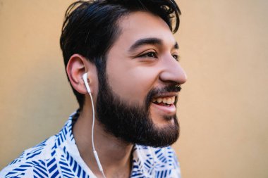 Yazlık kıyafetler giyen ve sarı arka planda kulaklıkla müzik dinleyen genç Latin adamın portresi..