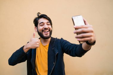Sarı duvara karşı mofil telefonuyla selfie çeken çekici bir gencin portresi. Teknoloji konsepti.