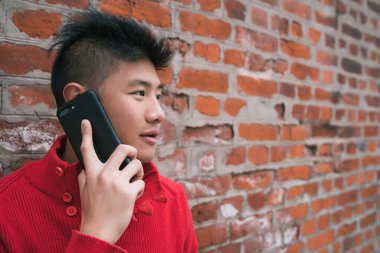Dışarıda, duvarın karşısında telefonla konuşan Asyalı genç bir adamın portresi. İletişim konsepti.