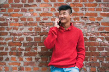 Dışarıda, duvarın karşısında telefonla konuşan Asyalı genç bir adamın portresi. İletişim konsepti.