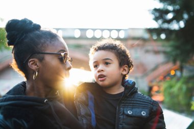 Afrika kökenli Amerikalı bir annenin portresi. Oğluyla parkta durmuş, eğleniyor. Monopental Ailesi.
