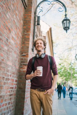 Sokakta yürüyen ve elinde bir fincan kahve tutan genç adamın portresi. Şehir konsepti.