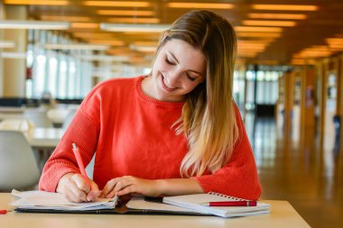 Üniversite kütüphanesinde okuyan genç bir öğrencinin portresi. Eğitim ve yaşam tarzı kavramı.