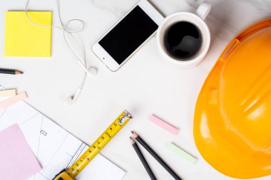 Planlara yakın çekim, mezura, bir fincan kahve ve sarı miğfer. Mühendis kavramı