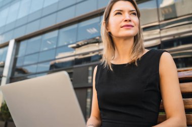 Sokakta otururken dizüstü bilgisayarını kullanan genç iş kadınının portresi. İş konsepti.