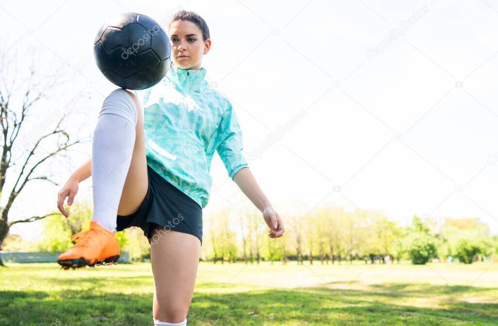Portrait of young woman practicing soccer skills and doing tricks with the football ball. Soccer player juggling the ball. Sports concept.