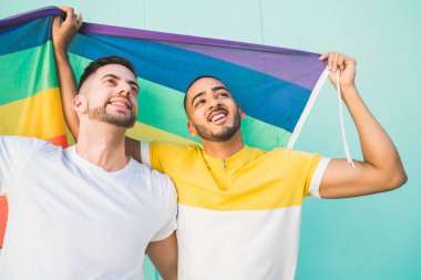 Sokakta gökkuşağı bayrağıyla sarılıp sevgilerini gösteren genç eşcinsel çiftin portresi. LGBT ve aşk konsepti