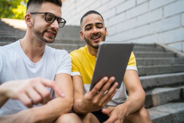 Mutlu eşcinsel çiftin birlikte vakit geçirdikleri ve merdivenlerde otururken dijital tablet kullandıkları portre. Lgbt ve Aşk Konsepti.