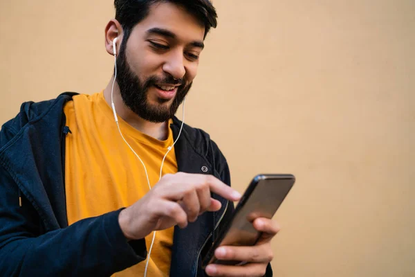 Portrét Mladého Latinskoamerického Muže Který Používá Svůj Mobilní Telefon Sluchátky — Stock fotografie