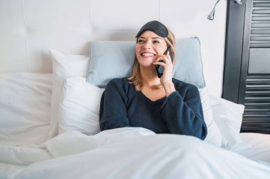Otel odasında yatakta yatarken telefonla konuşan genç bir kadının portresi. Seyahat ve yaşam tarzı kavramı.