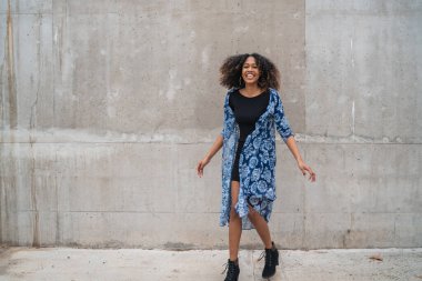 Gri duvarlara gülüp duran kıvırcık saçlı güzel Afro-Amerikan kadının portresi..