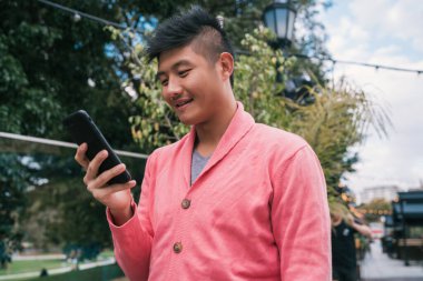 Sokakta cep telefonunu kullanan genç Asyalı adamın portresi. İletişim konsepti.