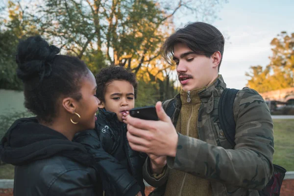 Portrait of lovely mixed race ethnic family having fun, relaxing and using mobile phone at the park outdoors.