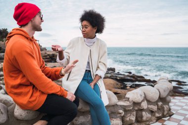 İki genç arkadaşın portresi, arka planda deniz otururken birlikte iyi vakit geçirip sohbet ediyorlar..