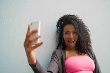 Mofili telefonuyla gri duvara selfie çeken afro kadın portresi. Teknoloji konsepti.