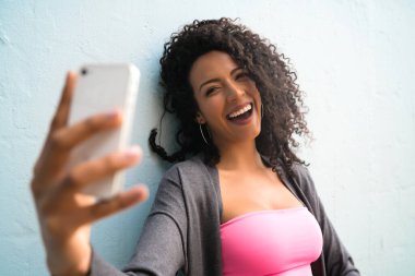 Mofili telefonuyla gri duvara selfie çeken afro kadın portresi. Teknoloji konsepti.