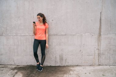 Eğitime ara verdiğinde cep telefonunu kullanan atletik bir kadının portresi. Spor ve sağlık yaşam tarzı.