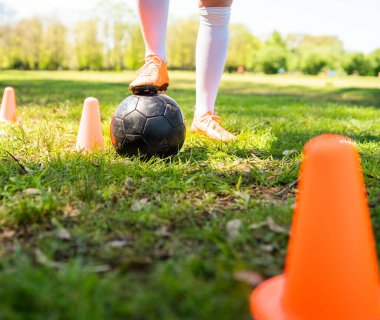 Genç bayan futbolcunun portresi sahada top oynarken koni etrafında koşuyor. Spor konsepti.