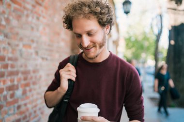 Sokakta yürüyen ve elinde bir fincan kahve tutan genç adamın portresi. Şehir konsepti.