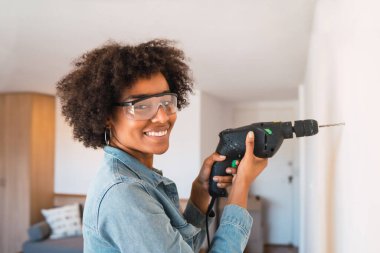 Evde elektrikli matkapla duvar delen genç afro kadın portresi. Ev geliştirme kavramı.