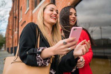 Sokakta cep telefonlarını kullanan iki genç arkadaşın portresi. Yaşam tarzı ve arkadaşlık kavramları.