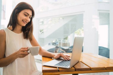 Bir kafede otururken dizüstü bilgisayarını kullanan genç Latin kadının portresi. Teknoloji ve yaşam tarzı kavramı.