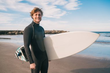 Genç sörfçü siyah sörf takımıyla okyanusta duruyor. Spor ve su sporları konsepti.