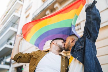 Sokakta gökkuşağı bayrağıyla kucaklaşan ve sevgilerini gösteren genç eşcinsel çiftin portresi. LGBT ve aşk konsepti