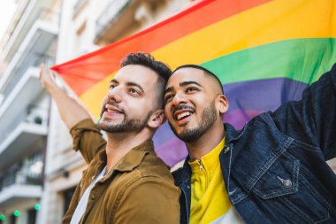 Sokakta gökkuşağı bayrağıyla kucaklaşan ve sevgilerini gösteren genç eşcinsel çiftin portresi. LGBT ve aşk konsepti