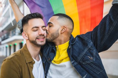 Sokakta gökkuşağı bayrağıyla kucaklaşan ve sevgilerini gösteren genç eşcinsel çiftin portresi. LGBT ve aşk konsepti