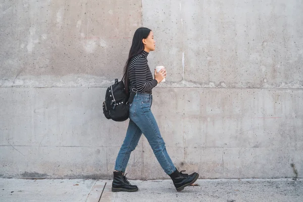 若いアジアの女性の肖像と灰色の壁に対するコーヒーカップを保持歩くと — ストック写真